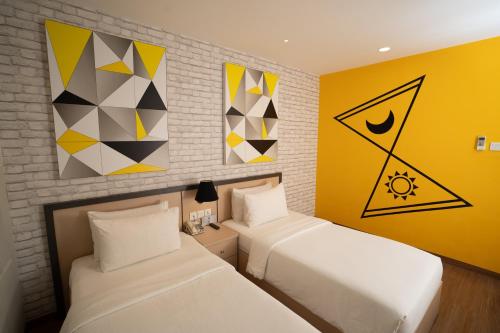 two beds in a room with yellow walls and paintings at Nite & Day Laguna Bintan in Tanjung Pinang
