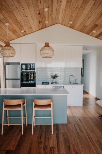 a kitchen with white cabinets and a blue island with two chairs at 3 Acres by the Moyne in Port Fairy