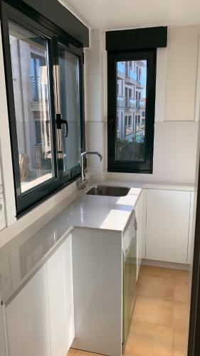 a white kitchen with a sink and two windows at Casa Galiñanes in Portonovo