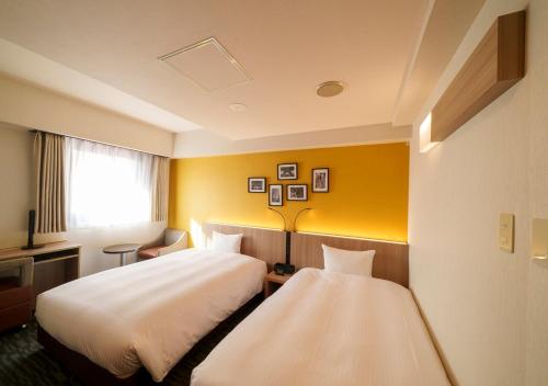 two beds in a hotel room with yellow walls at Smile Hotel Tokyo Asagaya in Tokyo