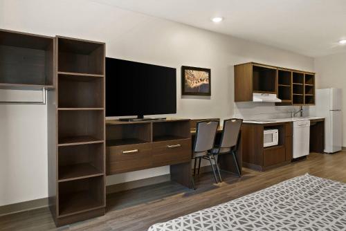 a room with a desk with a television and a kitchen at WoodSpring Suites East Lansing - University Area in East Lansing