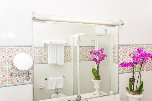 a bathroom with a sink and a mirror and purple flowers at Hotel Miramare in Lignano Sabbiadoro