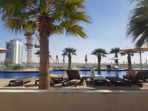 a swimming pool with chairs and palm trees in a resort at Cosy 1 Bedroom in Damac Hills | OFEX in Dubai