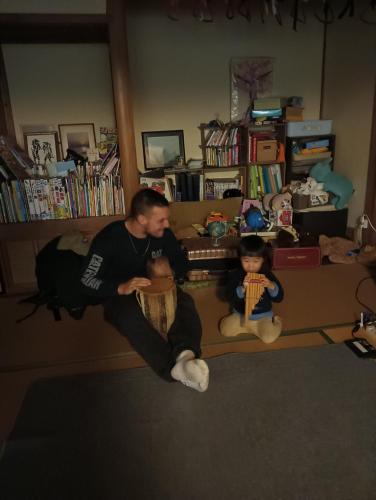 a man sitting in a living room with two dolls at Satoyama Guest House Couture in Ayabe