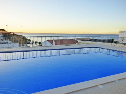 a large blue swimming pool with the ocean in the background at Apartamento Olhos D'Água in Albufeira