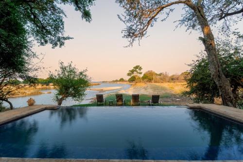 a swimming pool next to a river with chairs at Sian-simba-river-lodge in Victoria Falls