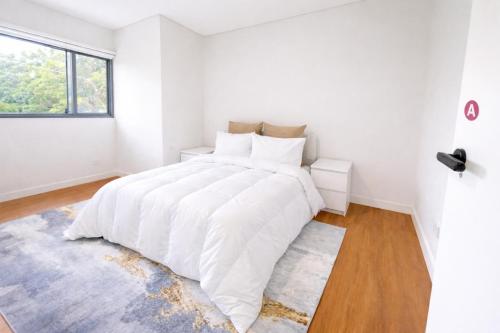 a white bedroom with a large bed with white sheets at ProHouse - Sydney Airport Wolli Creek in Sydney