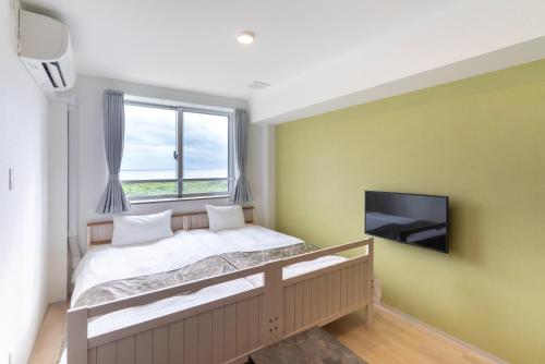 a bedroom with a bed and a tv on a wall at コート エトワレ マエザト-新築アパートメントホテル- in Ishigaki Island
