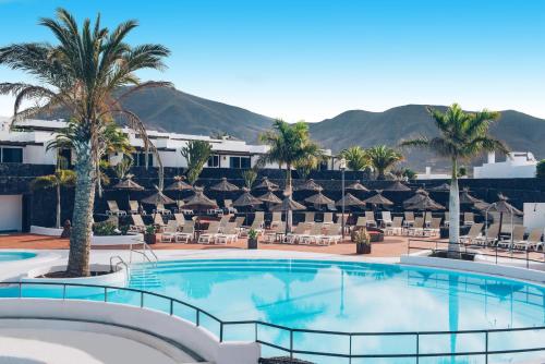 a pool at a resort with chairs and palm trees at Dream Bocayna Village in Playa Blanca