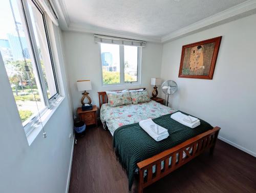 a bedroom with a bed with a green comforter and two windows at City/Valley Resort Apartment in Brisbane