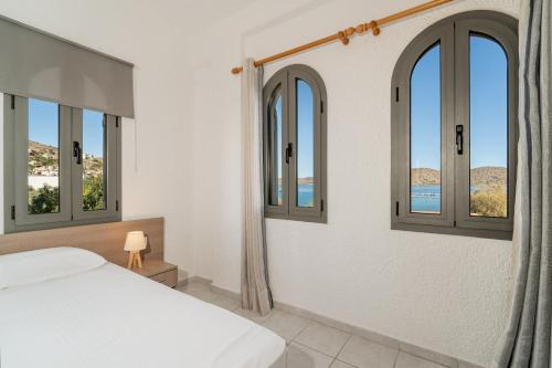 a bedroom with a bed and windows with a view of the ocean at Lena Apartments in Elounda