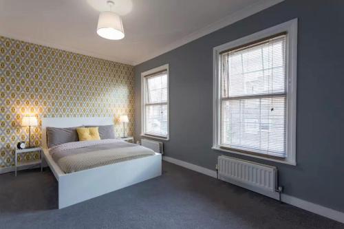 a bedroom with a white bed and two windows at Hastings House in Luton