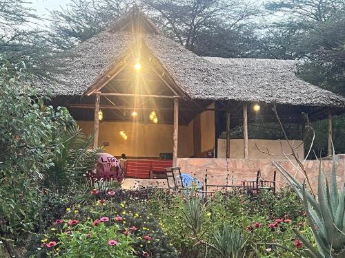 a house with a thatched roof with chairs and flowers at Mara Sunset Acacia Camp in Sekenani