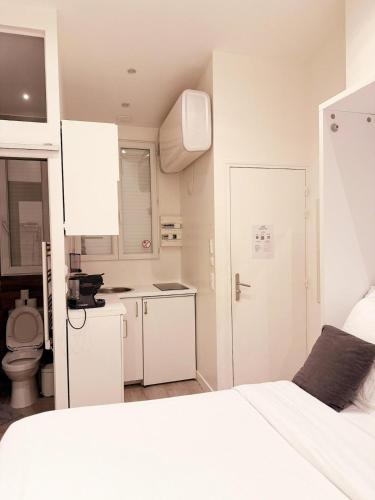 a white bedroom with a white bed and a kitchen at Rempart du Chateau-SV85 StudioVincennes in Vincennes