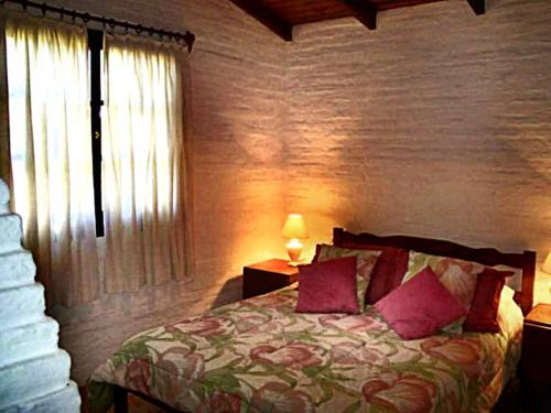 Un dormitorio con una cama con almohadas rosas y una ventana en Cabañas La Paloma, en La Paloma