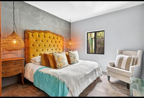 a bedroom with a bed with a yellow headboard and a chair at Beach House Living in Gordonʼs Bay
