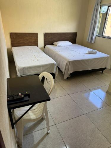 two beds in a room with a table and a desk at POUSADA FÊNIX in Viçosa