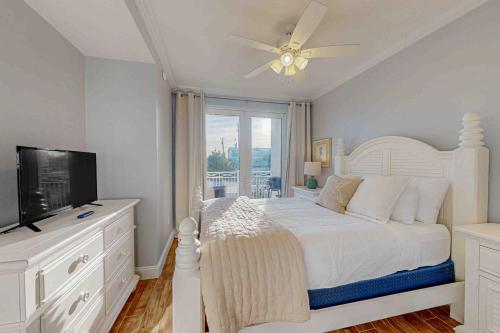 a white bedroom with a bed and a television at Tranquil Harbour 102 in Mexico Beach
