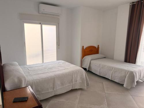 two beds in a white room with a window at Habitación Doble con Aire cerca de la Playa in Benidorm