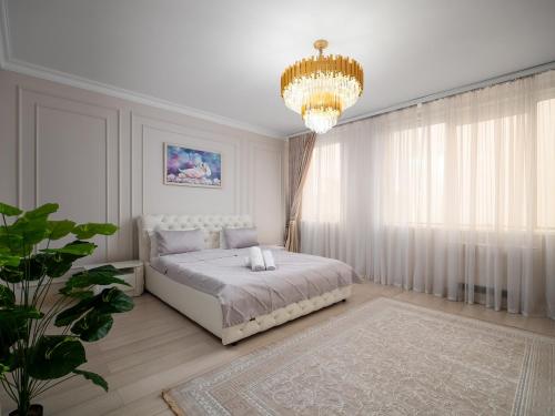 a white bedroom with a bed and a chandelier at Smart Lux 320 in Almaty