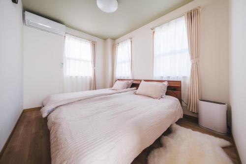 a bedroom with a bed with white sheets and windows at Genkido-Private House in Takasaki