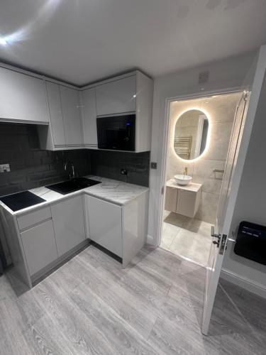 a kitchen with white cabinets and a sink and a mirror at Exclusive, newly built detached garden studio, private and self-contained, within family home grounds in Swanscombe