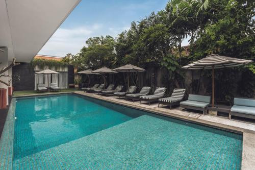 a swimming pool with chairs and umbrellas at Monolocale Resort & Spa Seminyak by Ini Vie Hospitality in Seminyak