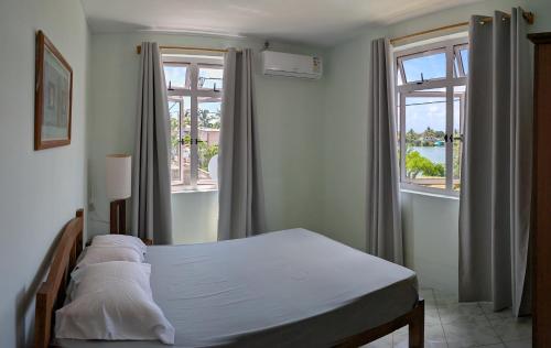 a bedroom with a bed and two windows at Desirella Villa APARTMENT in Mahébourg