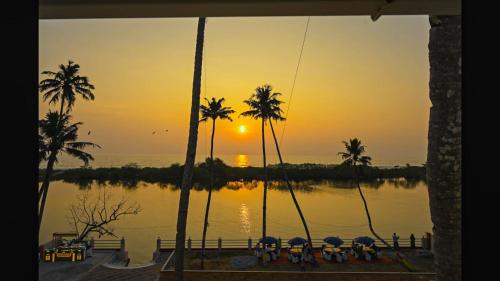 a sunset over a body of water with palm trees at Lake Star Beach Resort in Kappil