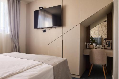 a bedroom with a bed and a desk with a tv on the wall at Garni Boutique Hotel Arta in Novi Sad