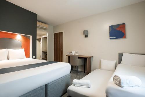 a hotel room with two beds and a desk at Ramada London Stansted Airport in Stansted Mountfitchet