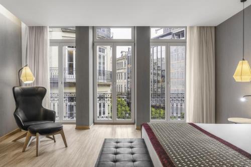 a bedroom with a bed and a chair and large windows at Eurostars Porto Centro in Porto