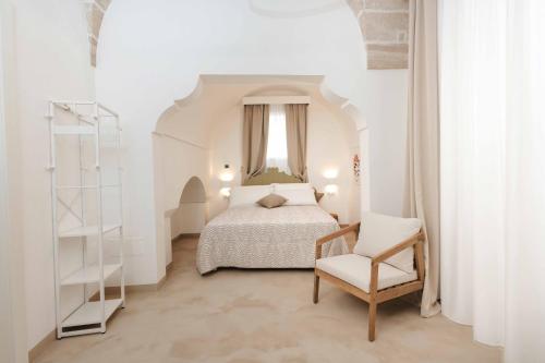 a white bedroom with a bed and a chair at Corte Vespro in Ugento