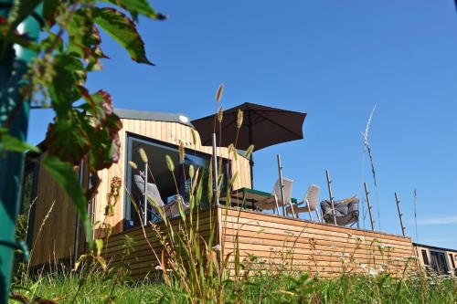 a house with chairs and an umbrella on top of it at Tinyhouse Seeträumchen direkt am See mit Terrasse für 4 in Bodenwöhr