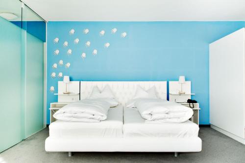 a bedroom with a white bed with a blue wall at Casinohotel Velden in Velden am Wörthersee