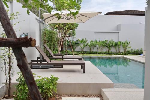 a pool with a chair and an umbrella next to a swimming pool at Botanica - Bali Style Luxury 3 BR Private Pool Villa in Ban Pak Lak