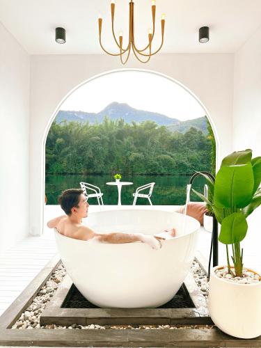 a man in a bath tub in a room with a window at Heaven Raft Erawan Floating Resort Romantic River View in Ban Mong Lai