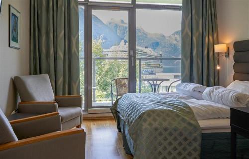 a bedroom with a bed and a chair and a large window at Havila Hotel Geiranger in Geiranger