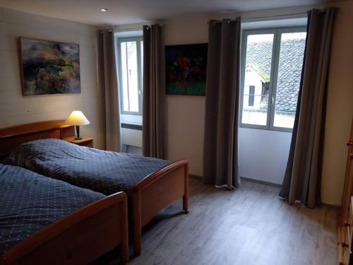 a bedroom with a bed and two windows at Maison Village Hautefage avec piscine chauffée in Hautefage