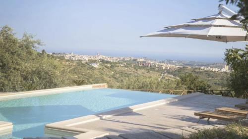 a swimming pool with an umbrella and a table and bench at Tenuta Olive Alive in Noto