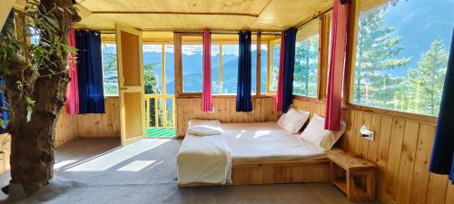 a bedroom with a bed in a room with windows at Jibhi Pine Nature Tree house in Jibhi