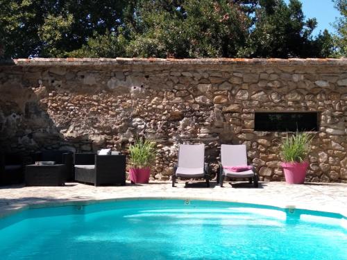 a pool with two chairs and a stone wall at Les feuillets de la Buire in Monteux