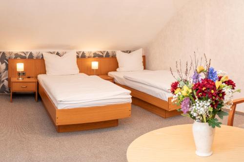 a hotel room with two beds and a vase of flowers at Hotel Waldhaus Waltershausen in Waltershausen