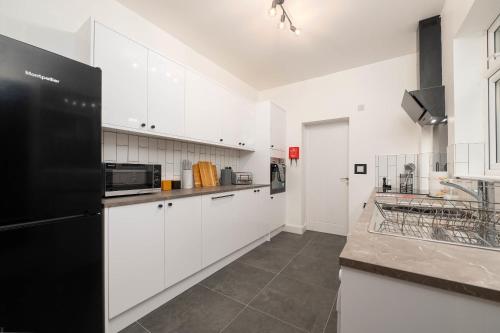a kitchen with white cabinets and a black refrigerator at Monks Quarters, Luxury 3 bed, Sleeps 6, PRIVATE PARKING x 2, Ideal for Groups & families, Prime location in Lincoln