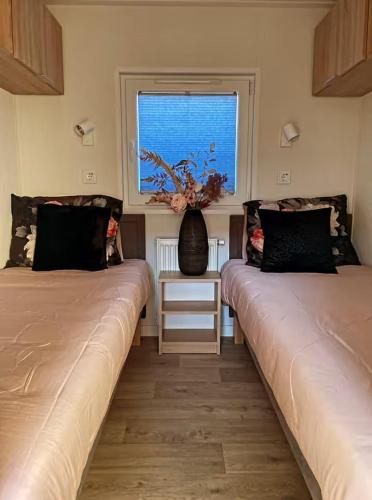 two beds in a room with a window and a vase at Chalet de Hofstee 118 in Nunspeet