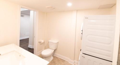 a white bathroom with a toilet and a refrigerator at New Basement Apartment with parking in Oakville