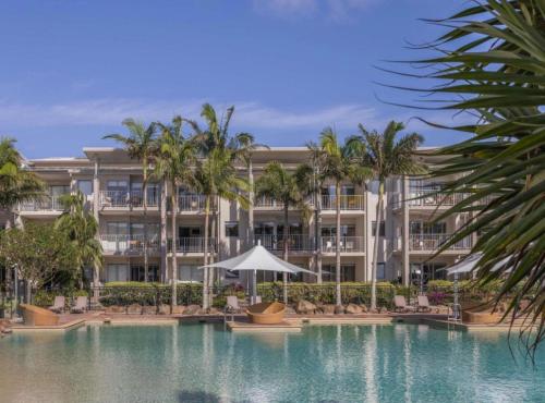 a large building with a swimming pool and palm trees at Peppers Salt Resort & Spa - Lagoon pool access 2 br spa suite in Kingscliff