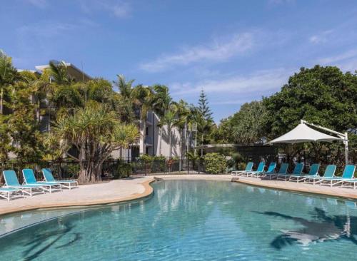 a swimming pool with blue lounge chairs and trees at Peppers Salt Resort & Spa - Lagoon pool access 2 br spa suite in Kingscliff