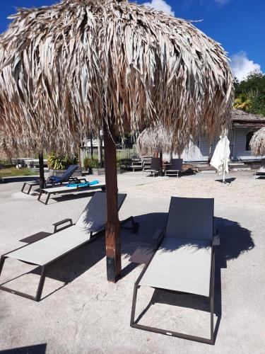 a group of lounge chairs under a straw umbrella at Diamantchery - Vue mer avec Deck privatif in Le Diamant