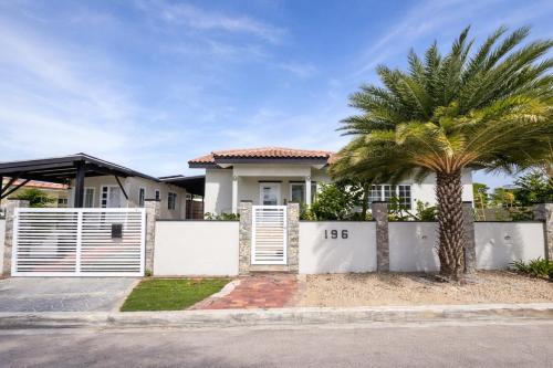 a house with a white fence and a palm tree at La Casita Torres in Oranjestad